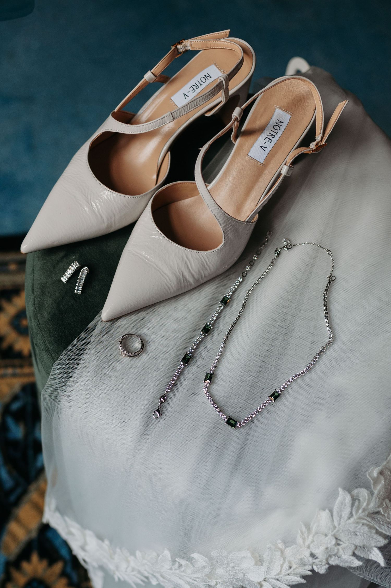 Cream pointed-toe slingback heels beside a crystal necklace, bracelet, earrings and ring resting on a lace-trimmed bridal veil.