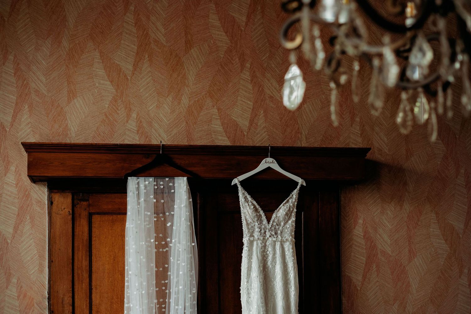 Details van trouwjurk en decor in een elegante binnenlocatie met kristallen kroonluchters, trouwfotograaf Brabant.