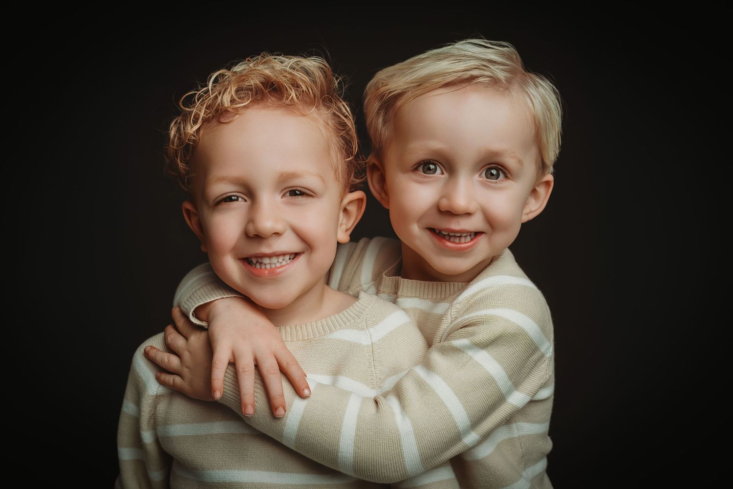 Close-up portret van broers/zussen in crème truien tegen donkere achtergrond, familieshoot Brabant