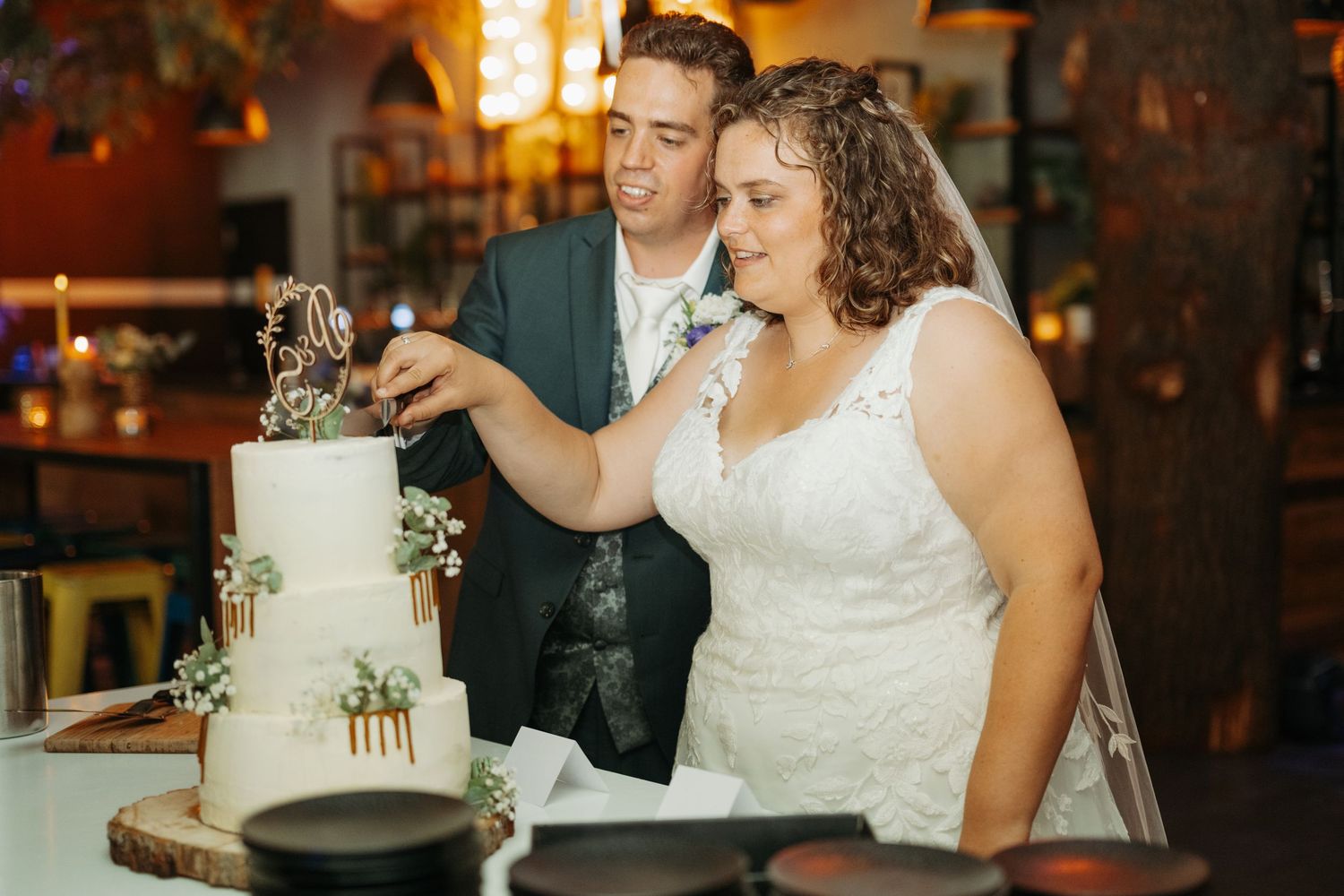Bride and groom cutting their white wedding cake decorated with greenery at their wedding reception.