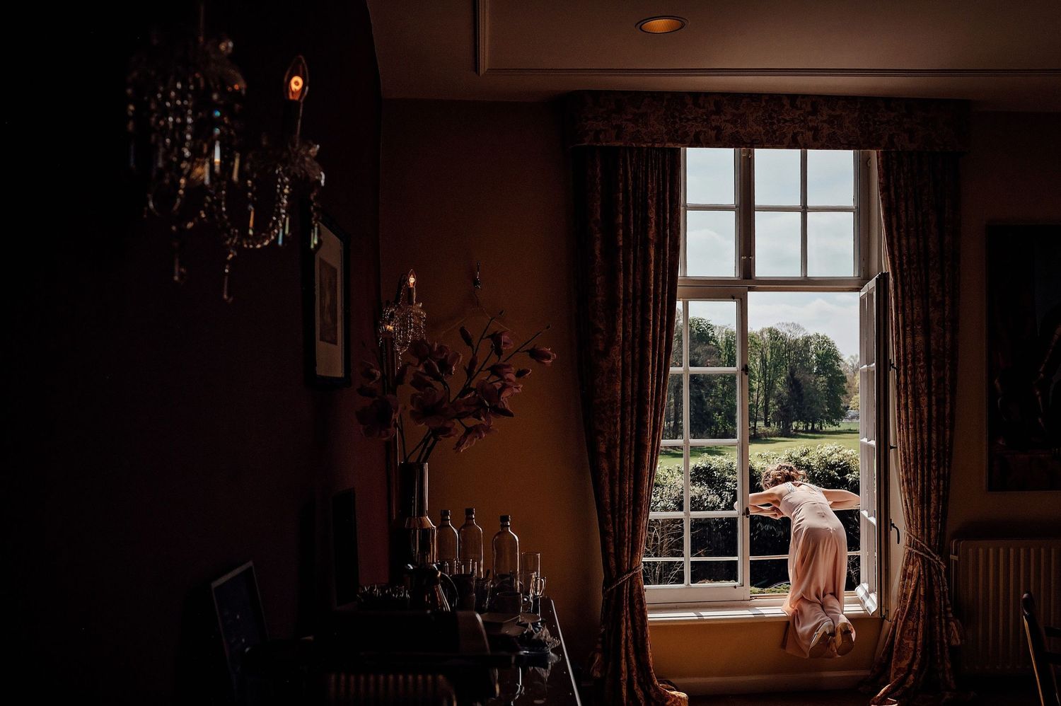 Elegant interieur met kroonluchter en groot raam met uitzicht op tuinlandschap, bruidsfotografie Den Bosch.