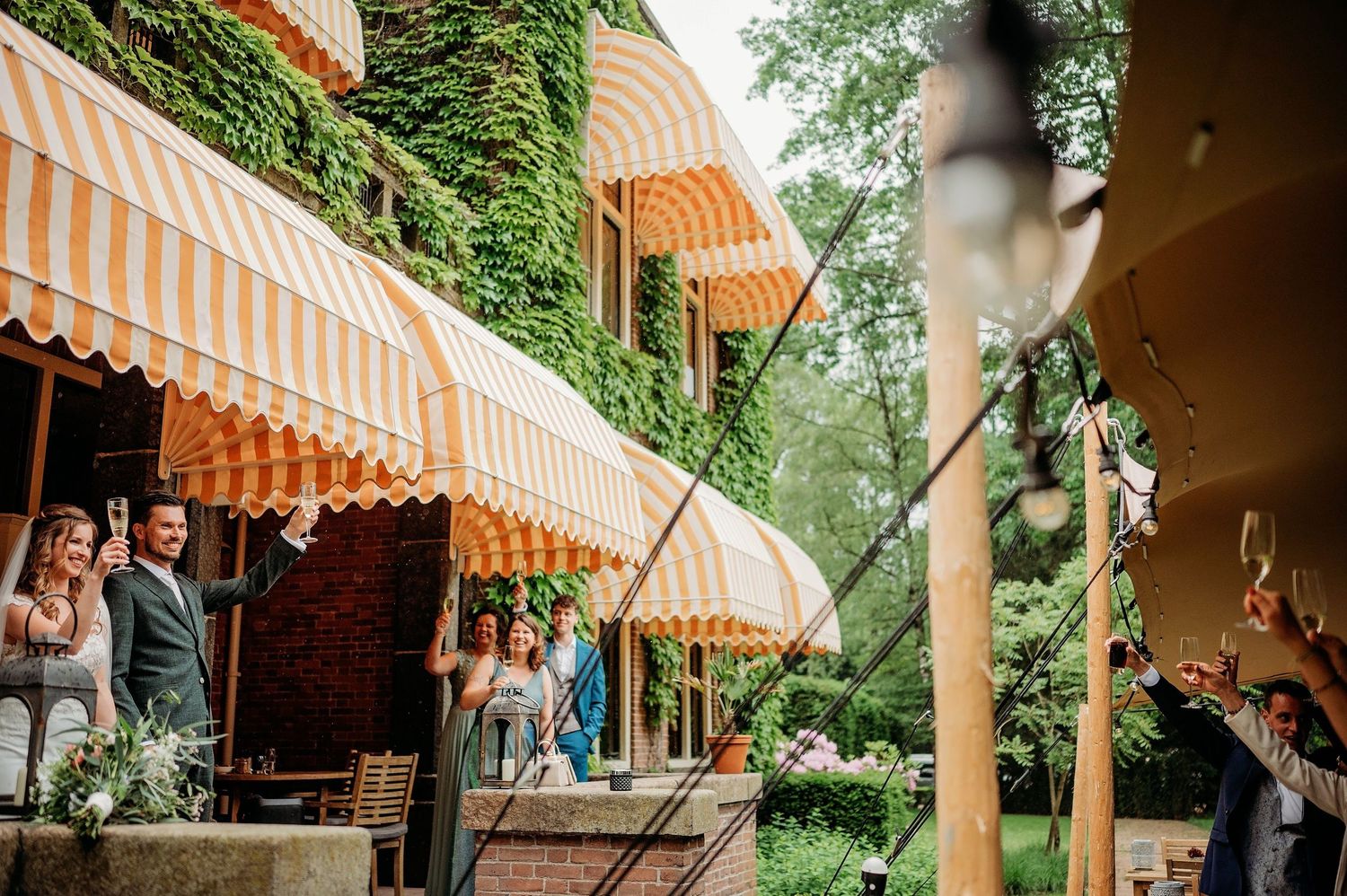 Wedding venue exterior featuring brick archways and striped awnings surrounded by greenery.
