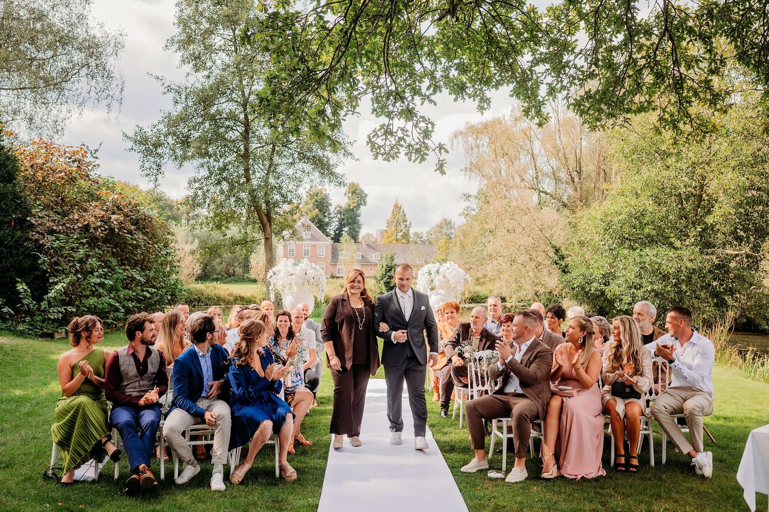 Bruidspaar loopt over boomlaan met zonlicht door bladeren, bruidsfotografie Kasteel Maurick Vught, Brabant.