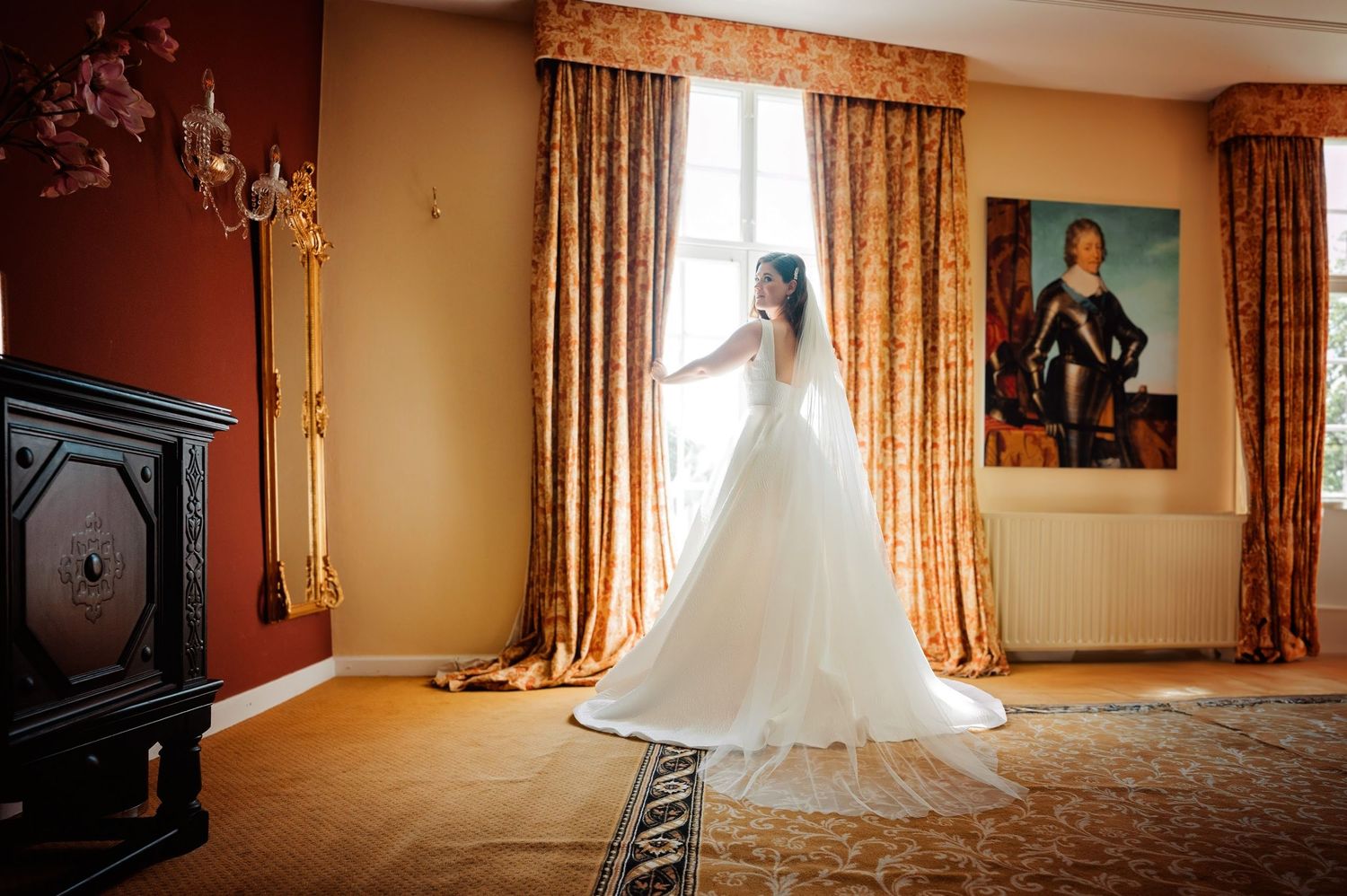 Trouwjurk elegant uitgestald in kamer met gouden licht en sierlijke meubels, bruidsfotografie Vught, Brabant.