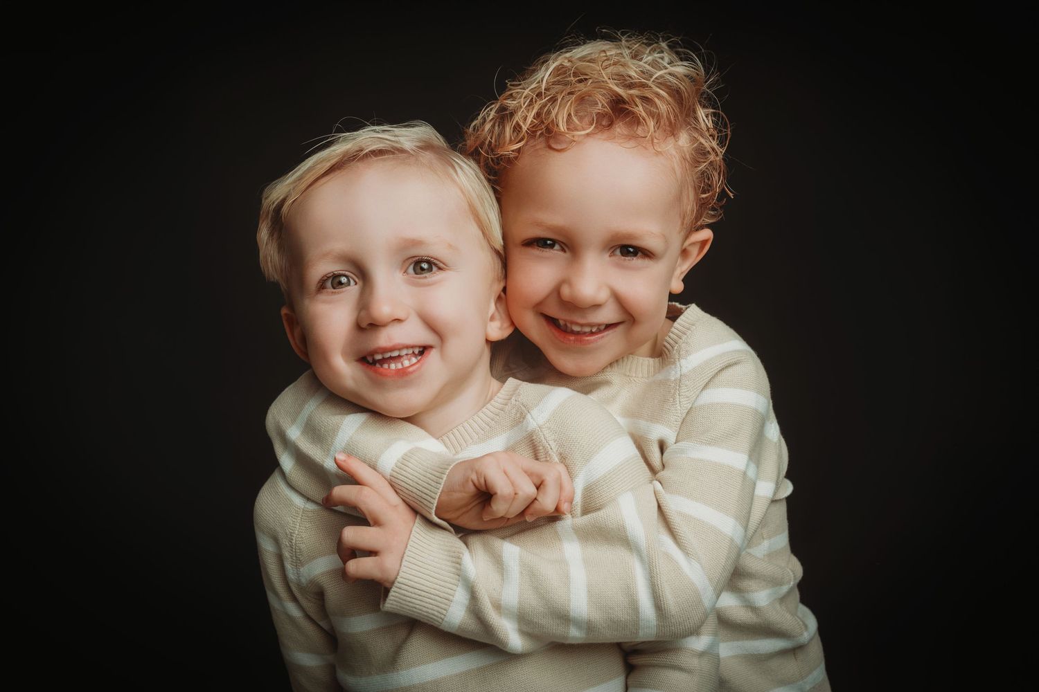 Kinderen in witte truien delen warme omhelzingen in studioportret, familieshoot Brabant