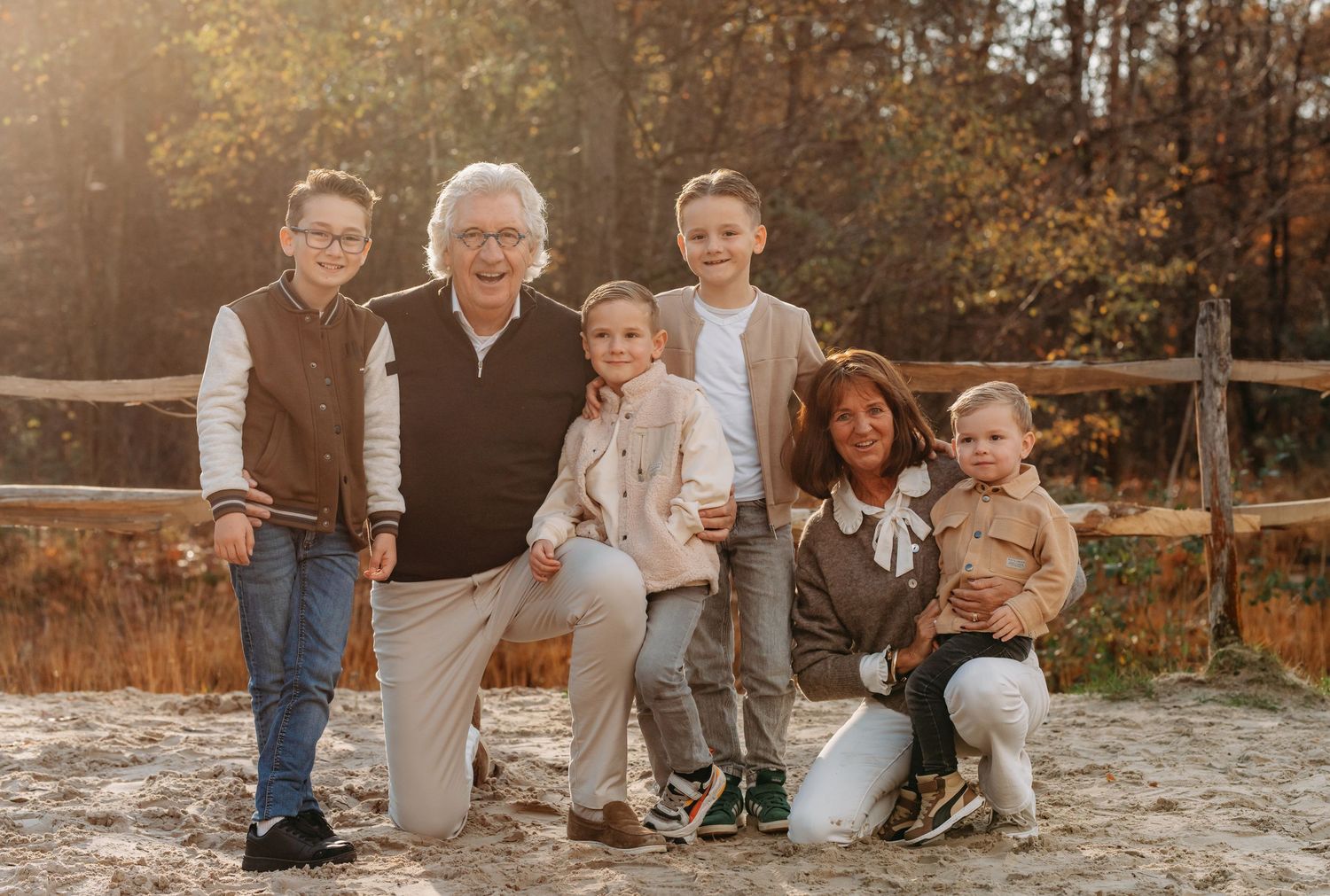 Family of six posing outdoors in autumn setting with warm golden light and rustic wooden fence backdrop.