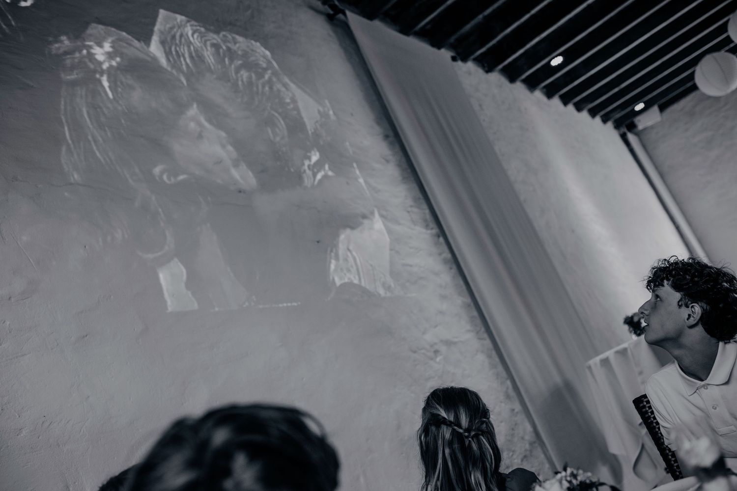 Black and white photo of people viewing a large projected image on a wall at an indoor event.