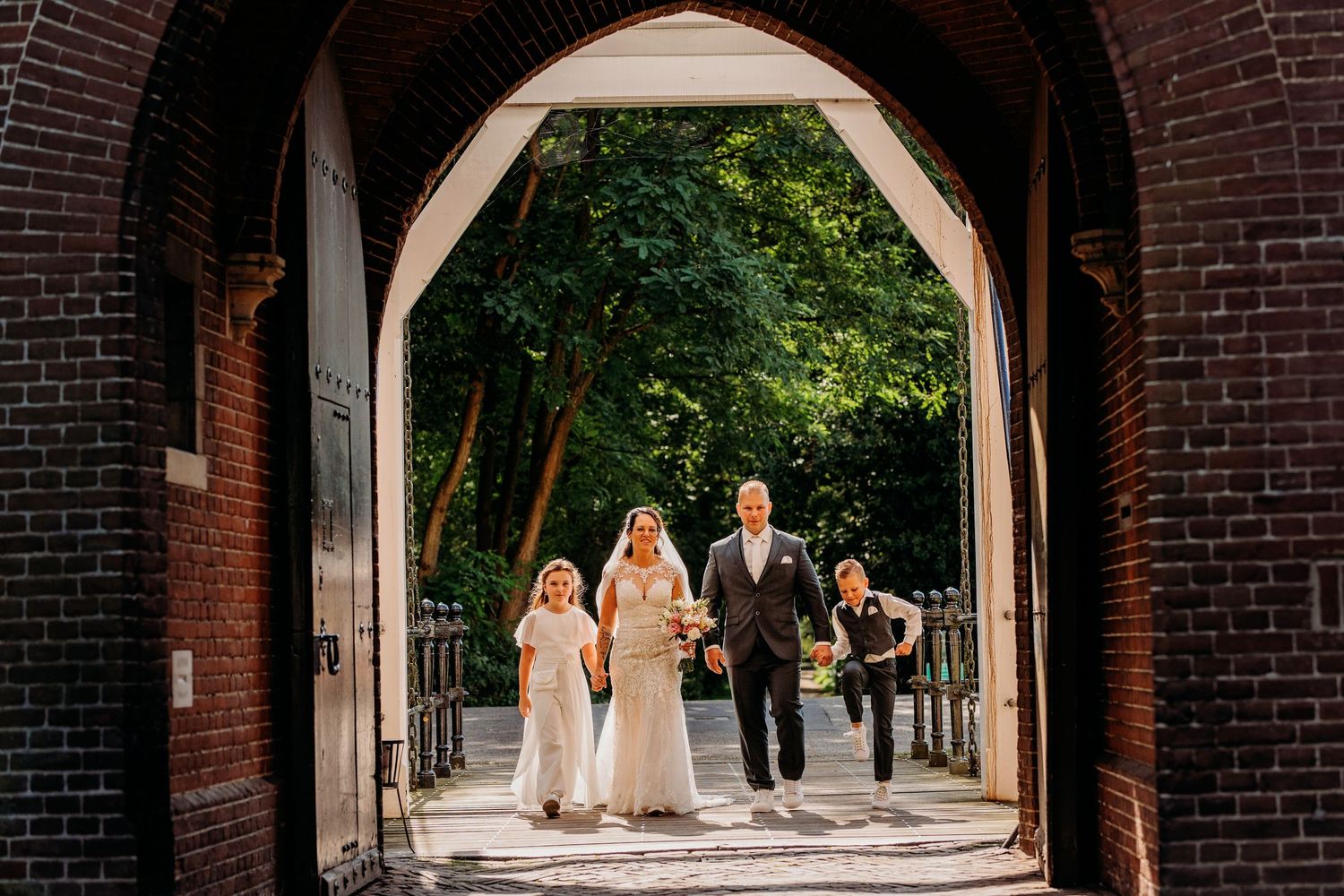Bruidspaar loopt door bakstenen boog in tuin, bruidsfotografie Kasteel Maurick Vught, Brabant.