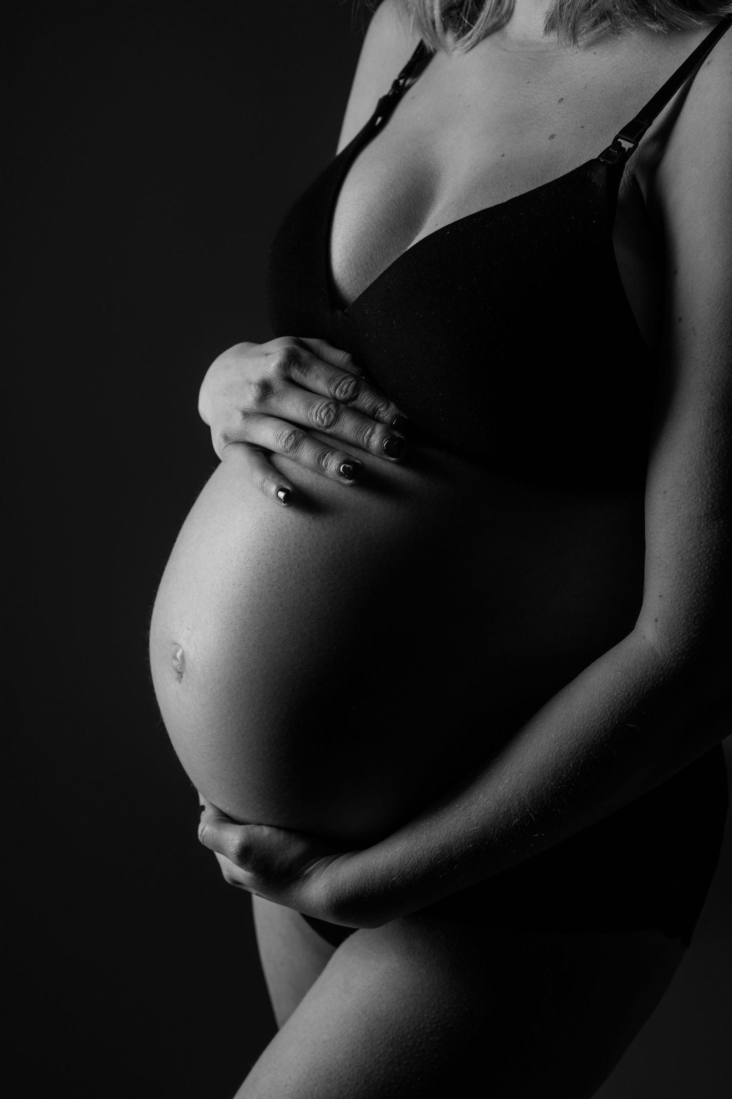 Zwart-wit artistieke zwangerschapsfoto van buik silhouet tegen donkere achtergrond, zwangerschapsfotografie Brabant.