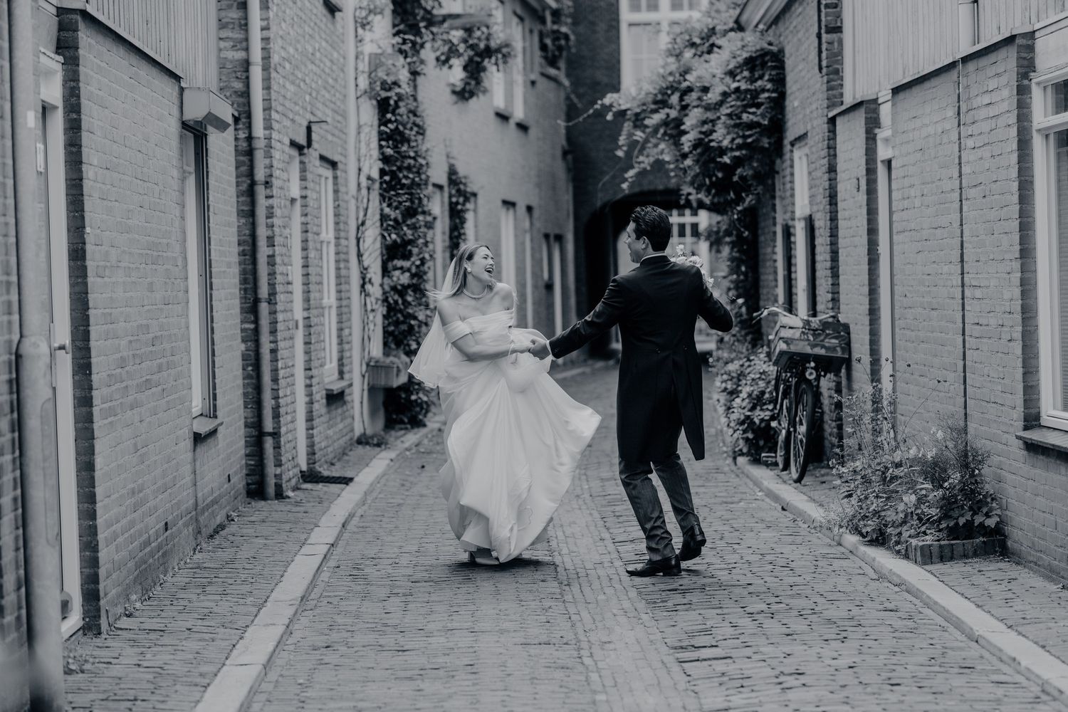 Bruid en bruidegom wandelen hand in hand over charmant kasseienstraatje op trouwdag, bruidsfotografie Brabant