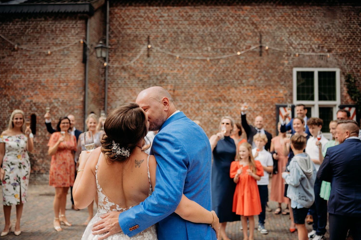 Bride and groom share a kiss while guests celebrate at an outdoor wedding reception.
