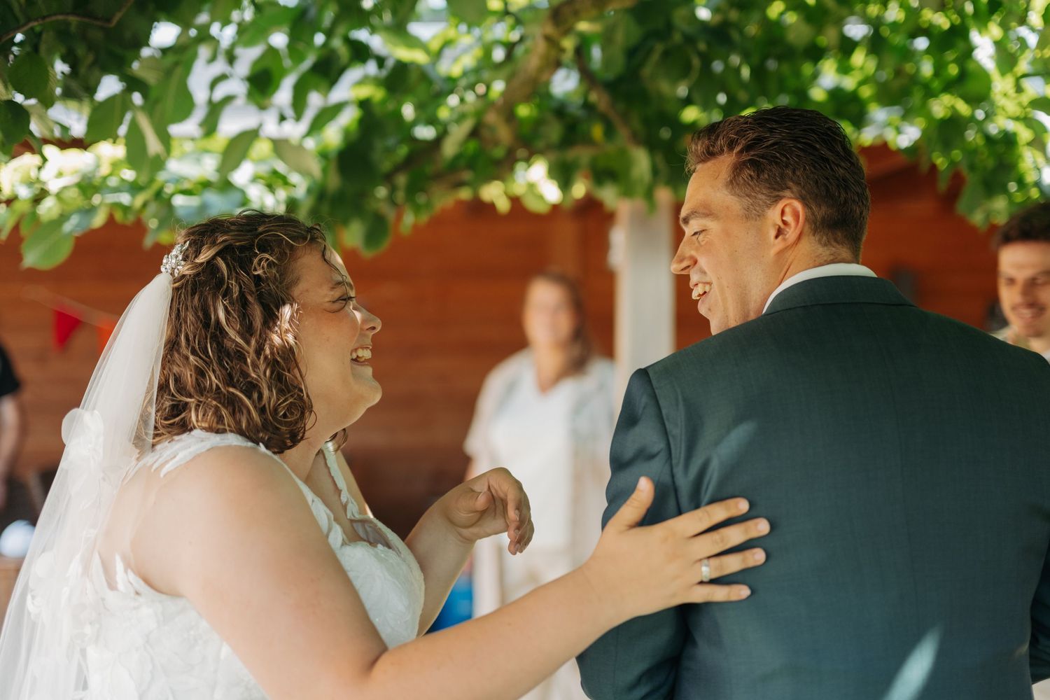 Bride and groom share a joyful moment during outdoor wedding ceremony, bride in white dress smiling at groom in suit.