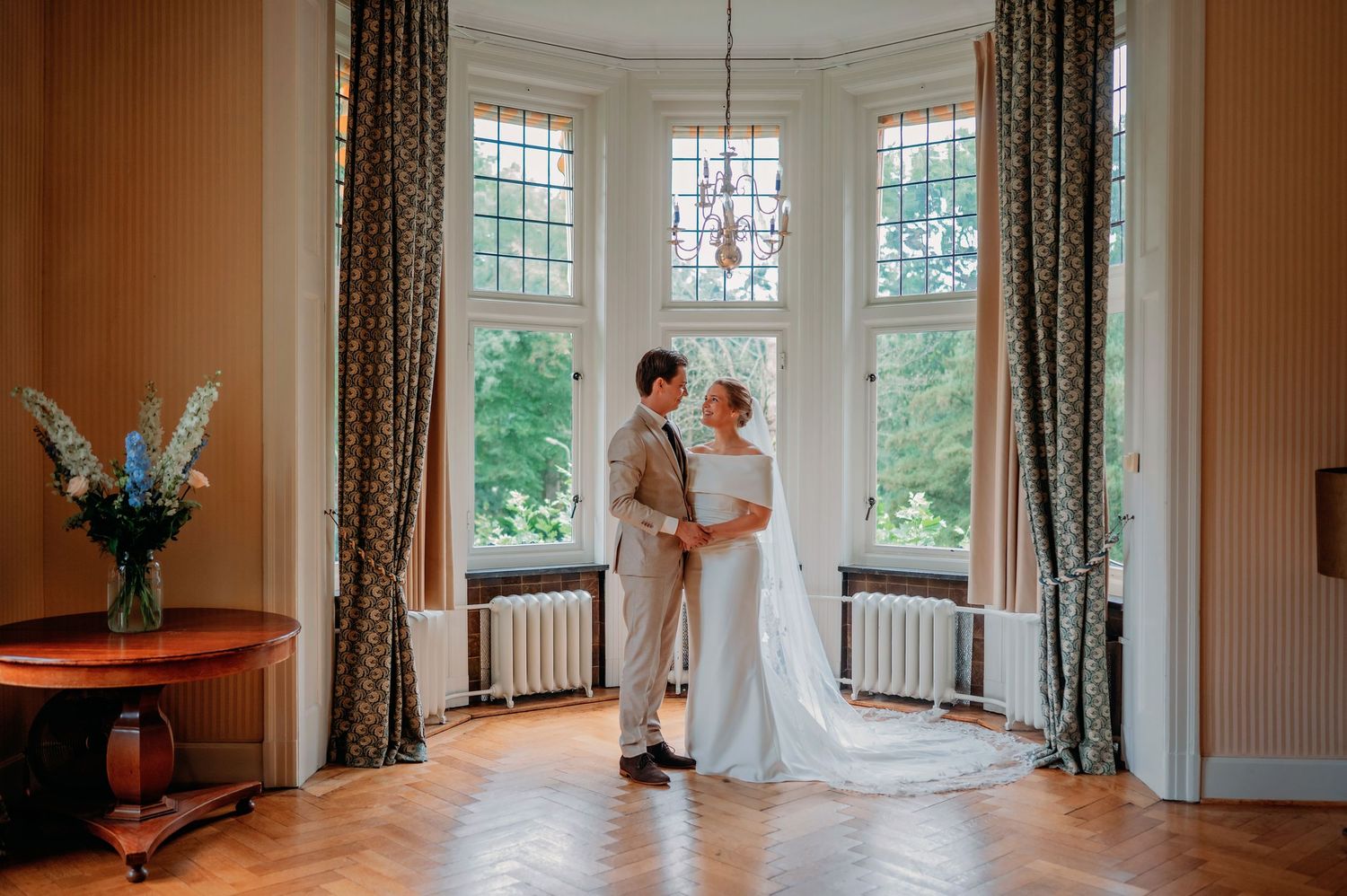 Bride and groom share a romantic moment in an elegant bay window room with herringbone floors.
