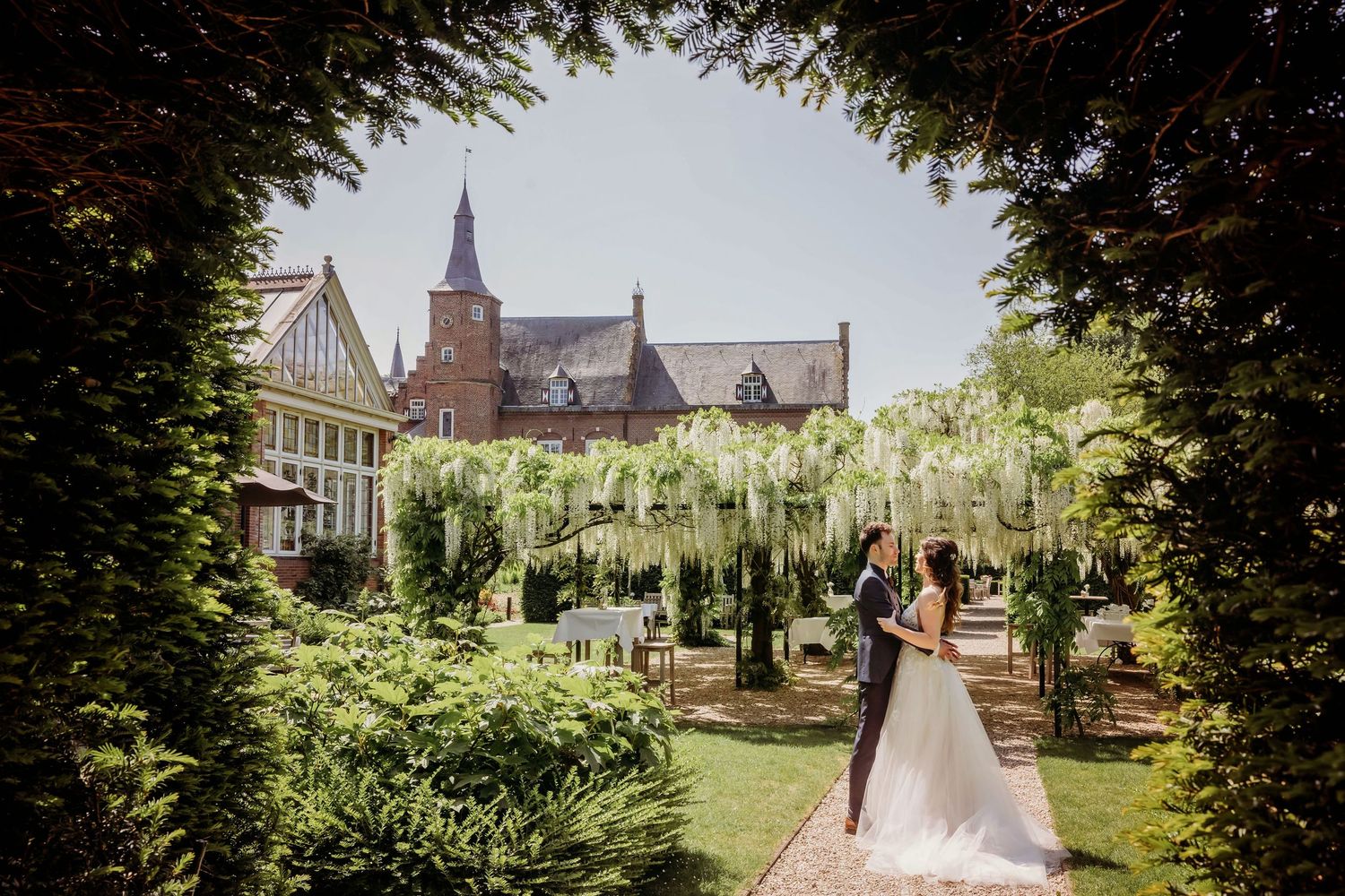 Bruidspaar bij kerk met stenen architectuur en verzorgde tuinen in zomer, bruidsfotografie Kasteel Maurick Vught, Brabant.