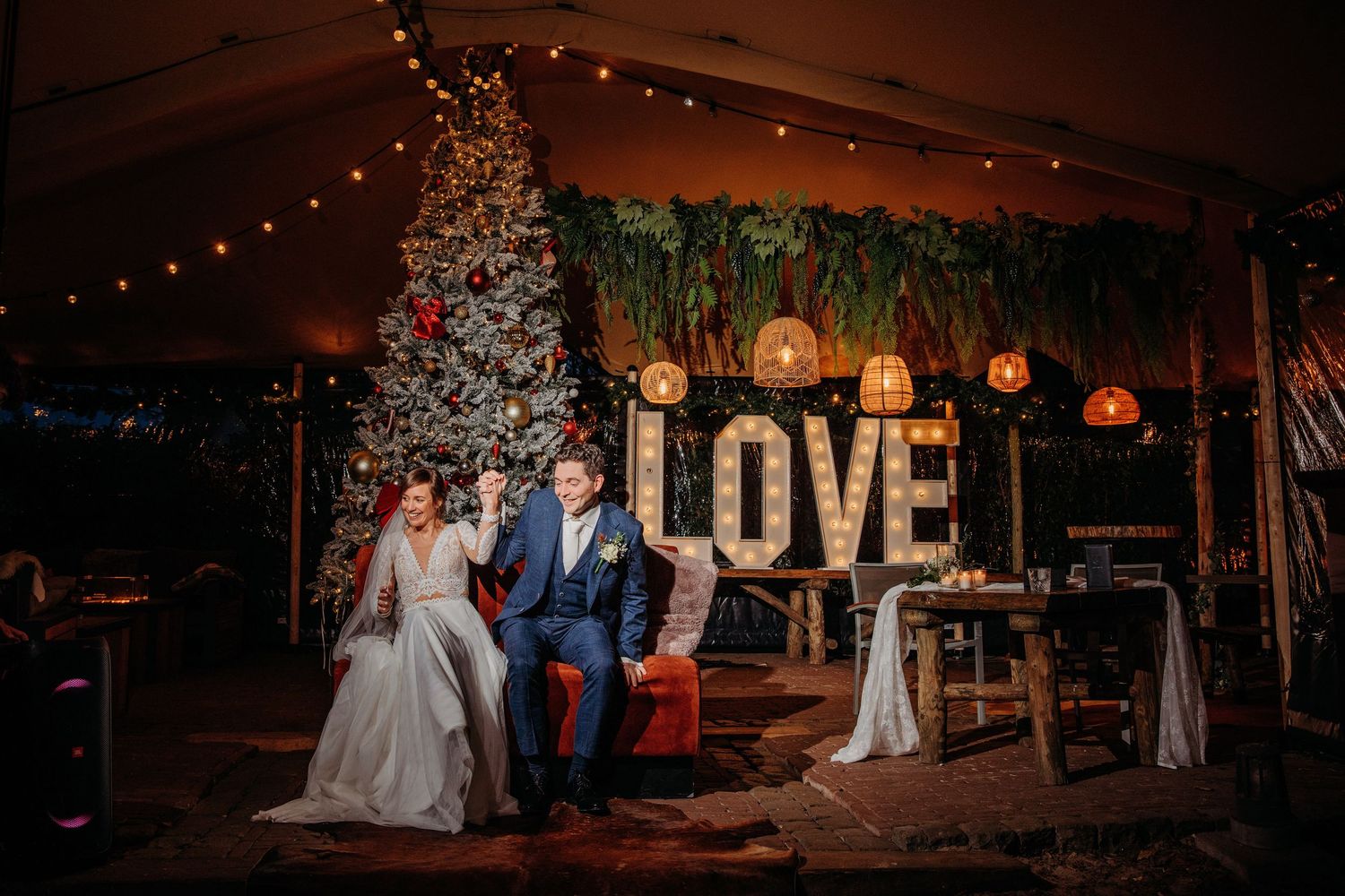 Bruidspaar poseert bij LOVE letters en kerstboom, romantische bruidsfotografie bij Boscafé Oisterwijk, regio Brabant.