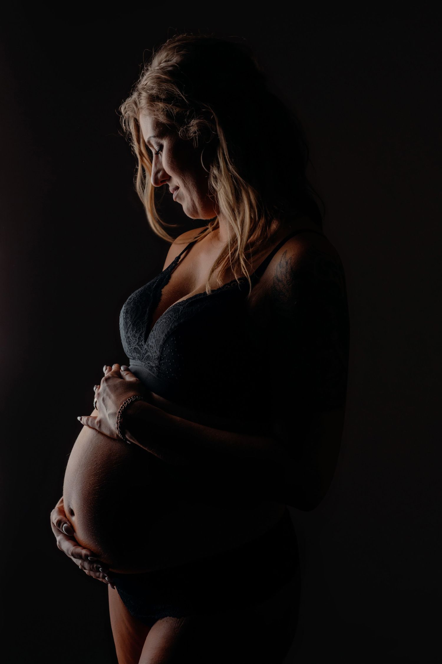 Dramatische low-key zwangerschapsfoto met nadruk op silhouet in zwarte kanten jurk, zwangerschapsfotografie Brabant