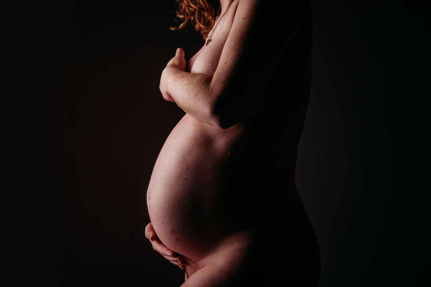 Artistiek silhouet van zwangere buik tegen donkere achtergrond, zwangerschapsfotografie Brabant