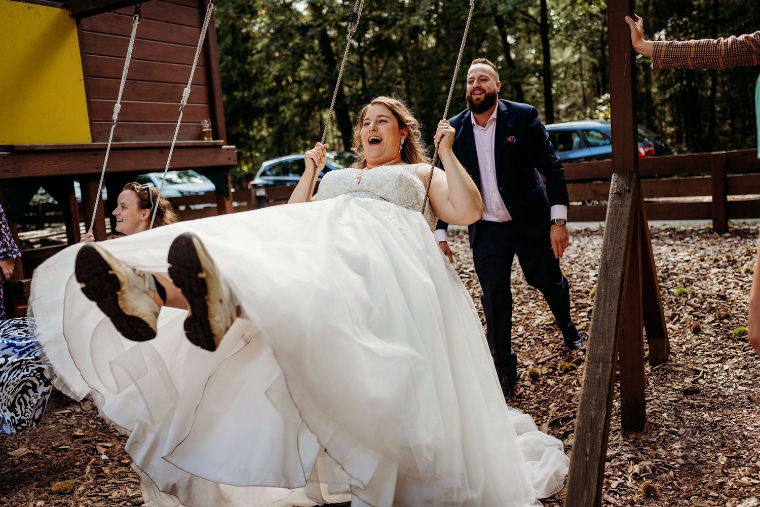 Speelse momenten op houten schommels in trouwkleding bij buitenevenement, bruidsfotografie Brabant