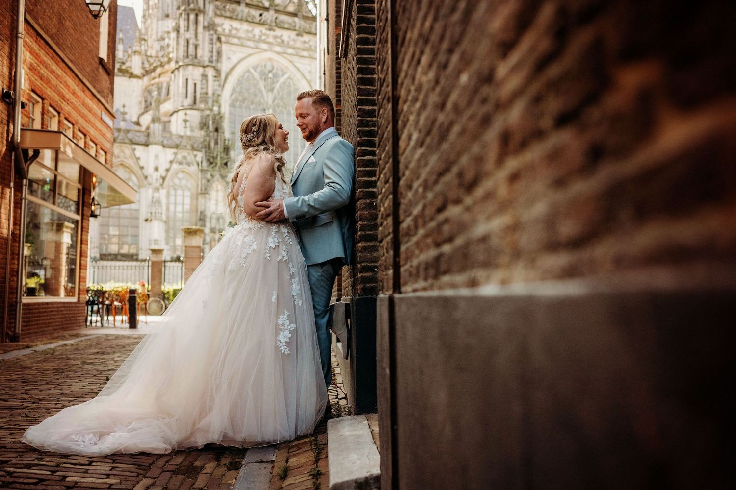 Romantische trouwfoto bij bakstenen muur met torens op achtergrond, bruidsfotografie in Den Bosch en omgeving Brabant.