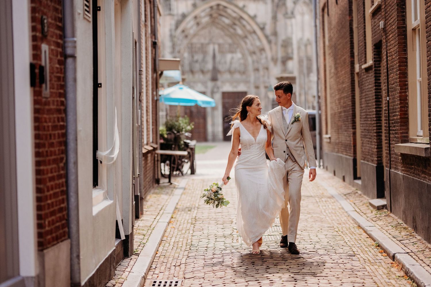 Bruidspaar loopt door sfeervol steegje in binnenstad Den Bosch, romantische trouwshoot en bruidsfotografie in Brabant.