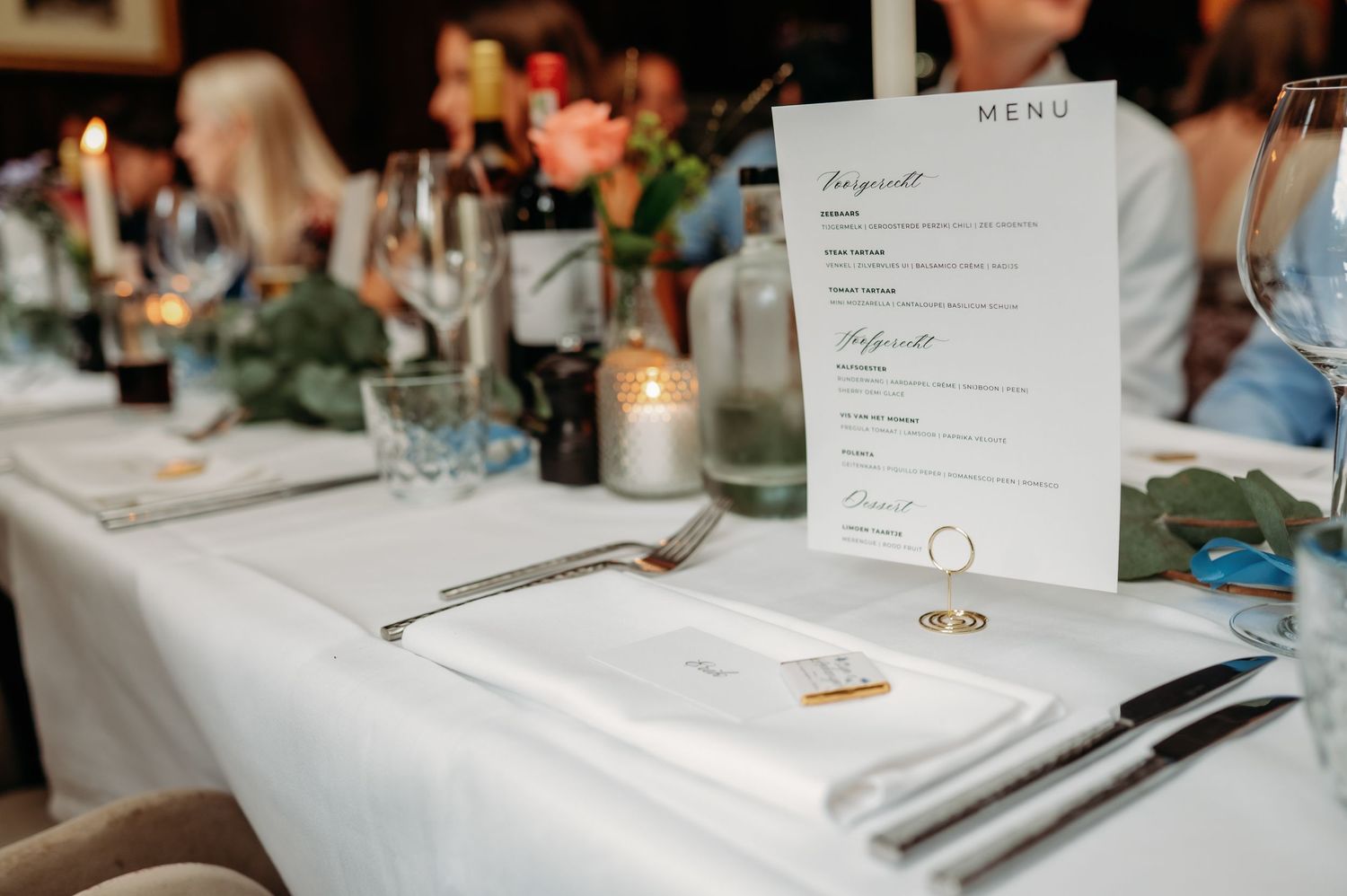 Elegant wedding table setting with white linen, candles, floral centerpiece, and a printed dinner menu card.