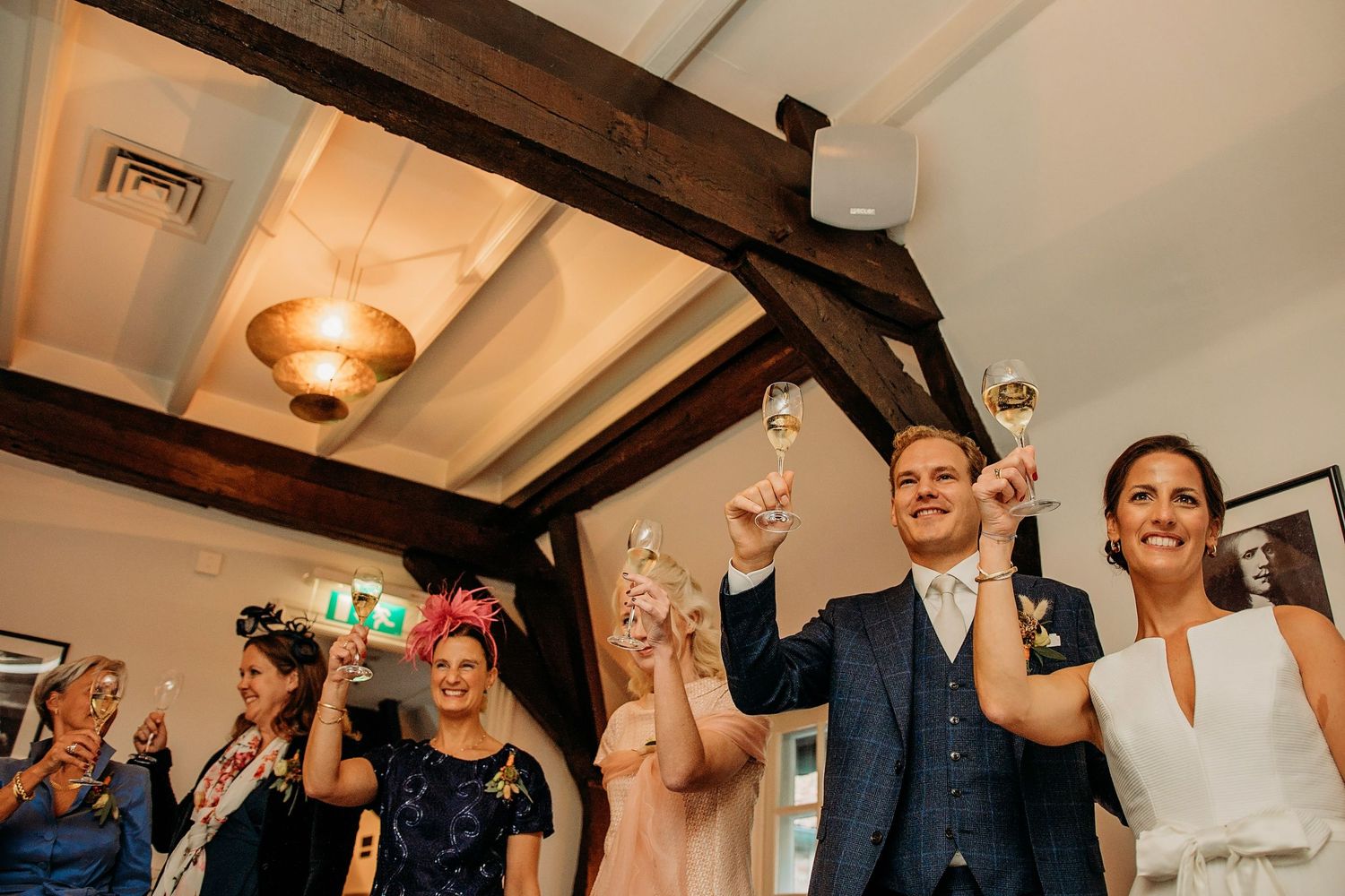 Gasten heffen champagneglazen onder rustieke houten balken, bruidsfotografie Kasteel Maurick Vught, Brabant.
