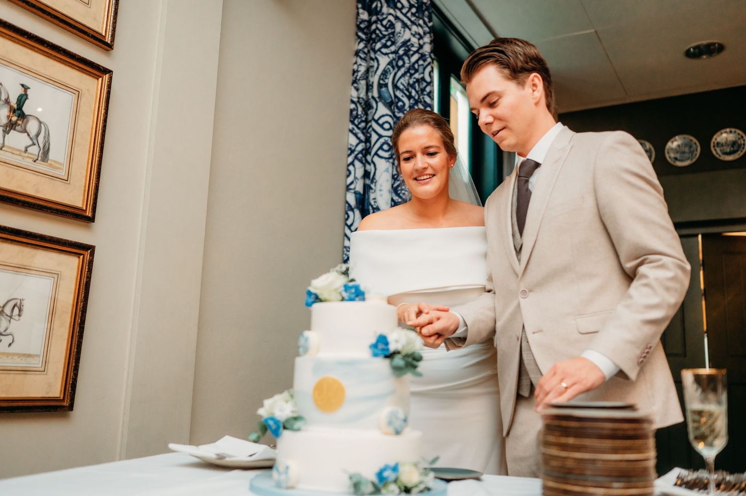 Bride and groom cut white wedding cake decorated with blue flowers at elegant reception.