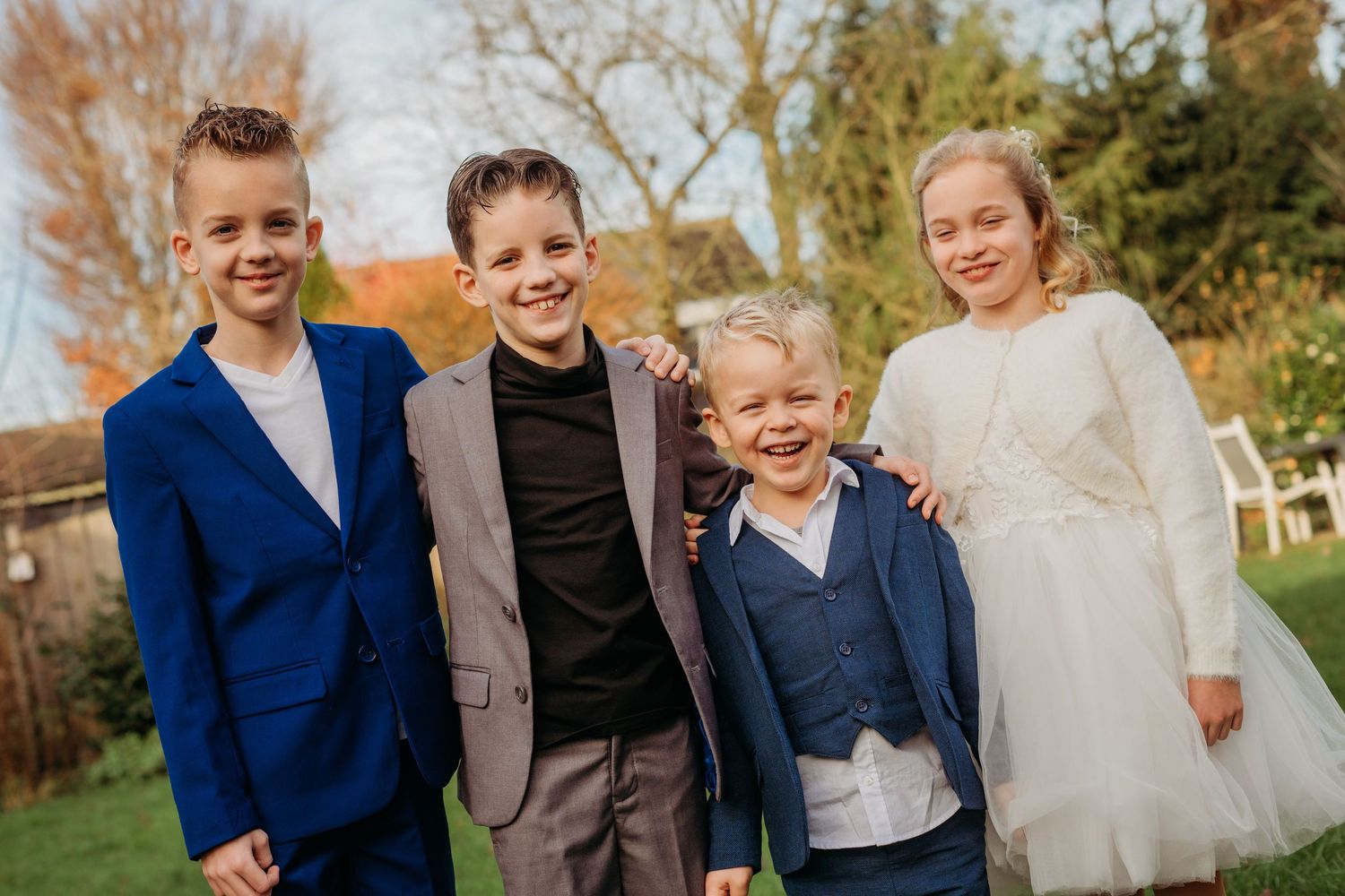 Vier gasten in formele kleding lachen samen buiten op herfstdag, spontane bruidsfotografie bij Boscafé Oisterwijk, Brabant.
