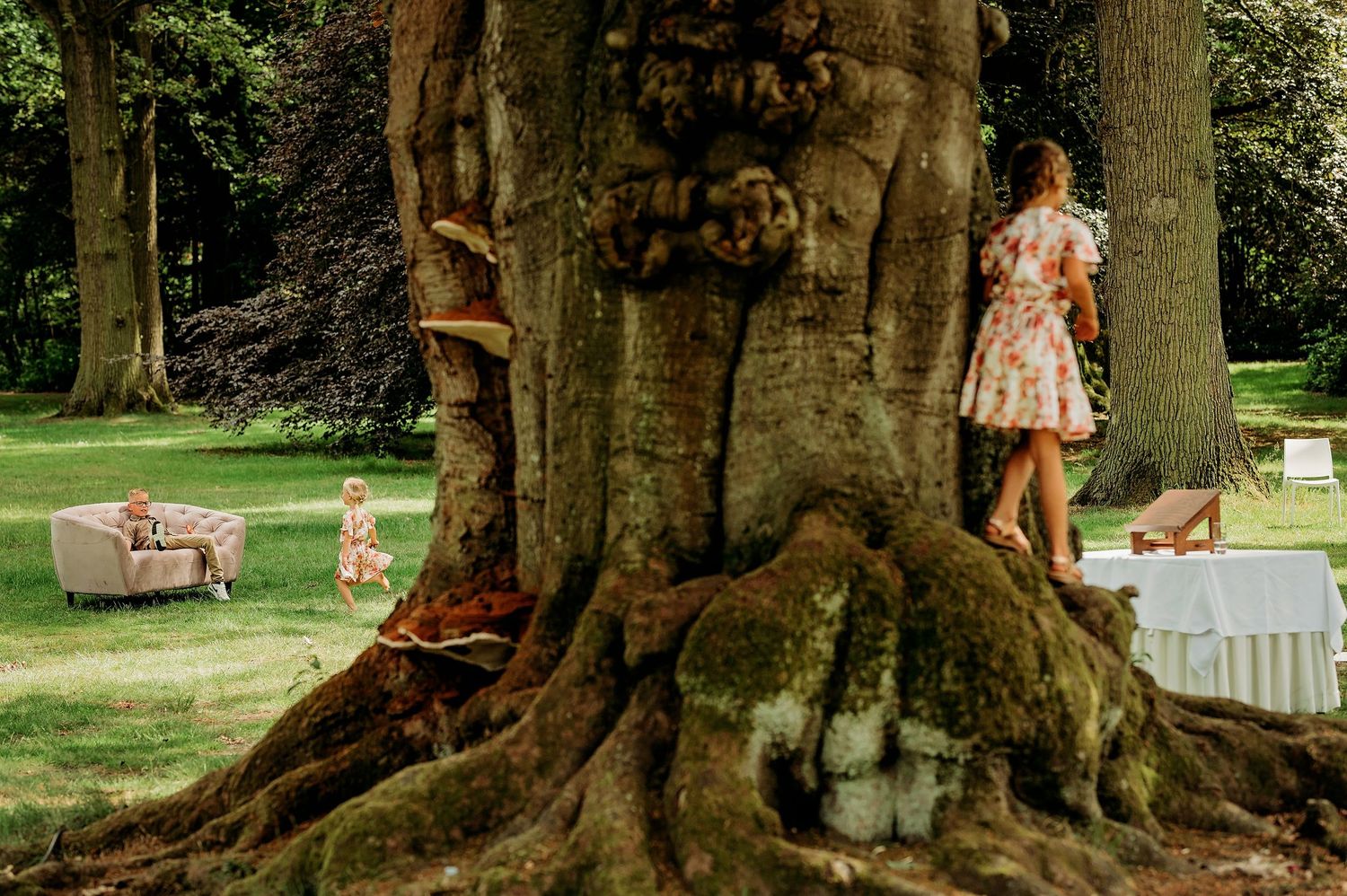 Bruidsfeest geniet van spontane momenten onder grote volwassen bomen in parksetting, bruidsfotografie Brabant