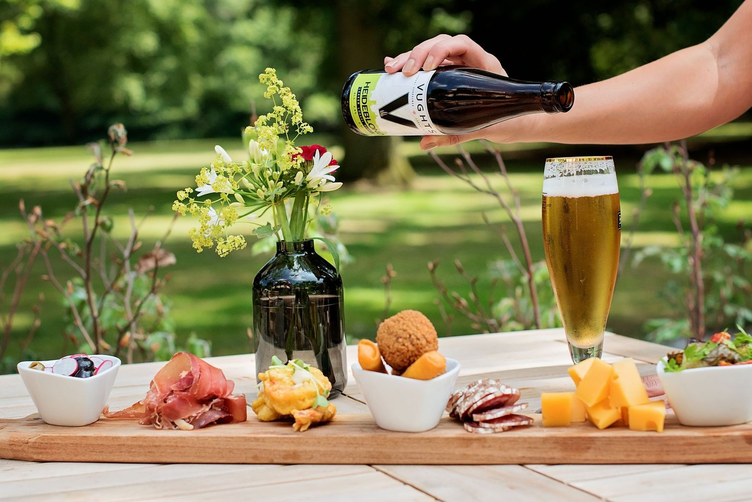 Buitendining spread met wijn, kaas en hapjes op houten tafel in tuin, foodfotografie Brabant