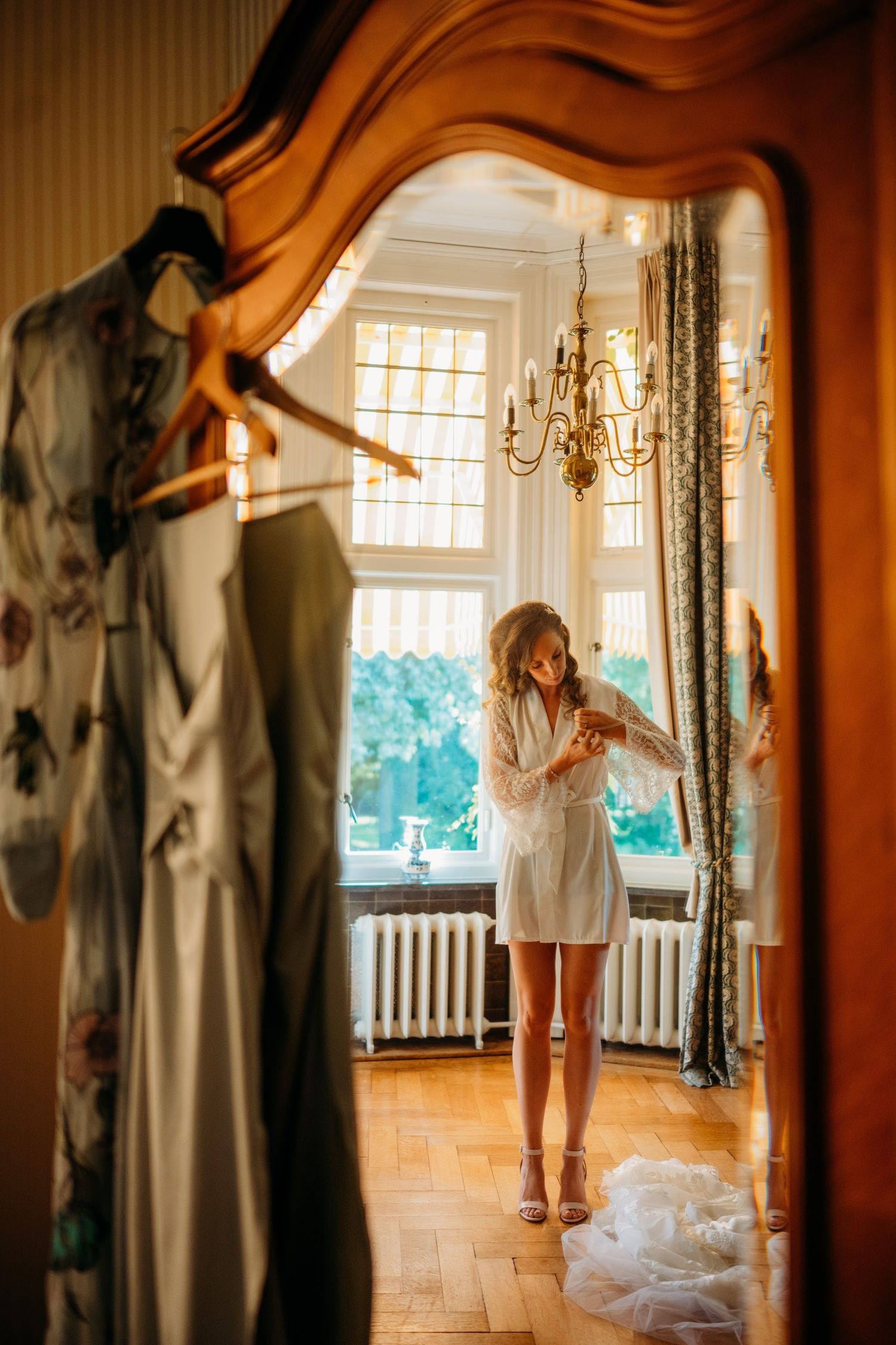 Zonslicht stroomt door ramen bij bruid in vintage kamer met kroonluchter, sfeervolle bruidsfotografie Huize Bergen Vught, Brabant.