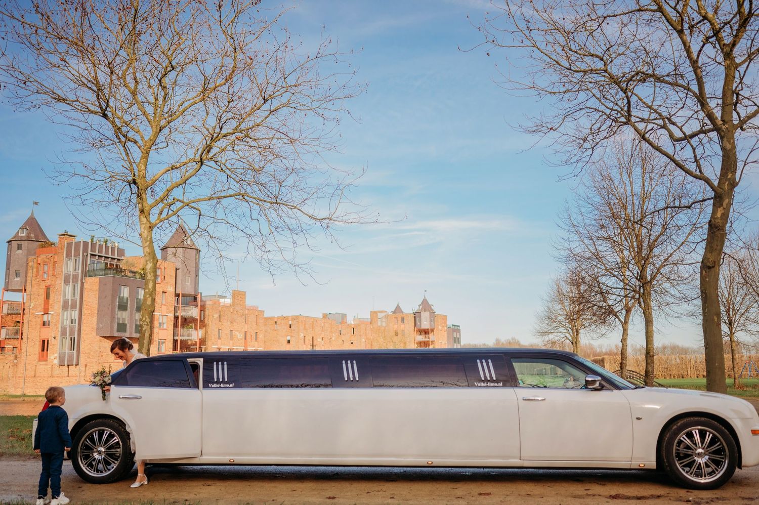 Witte limousine geparkeerd bij historische bakstenen panden op zonnige winterdag, bruidsfotografie bij Boscafé Oisterwijk, Brabant.