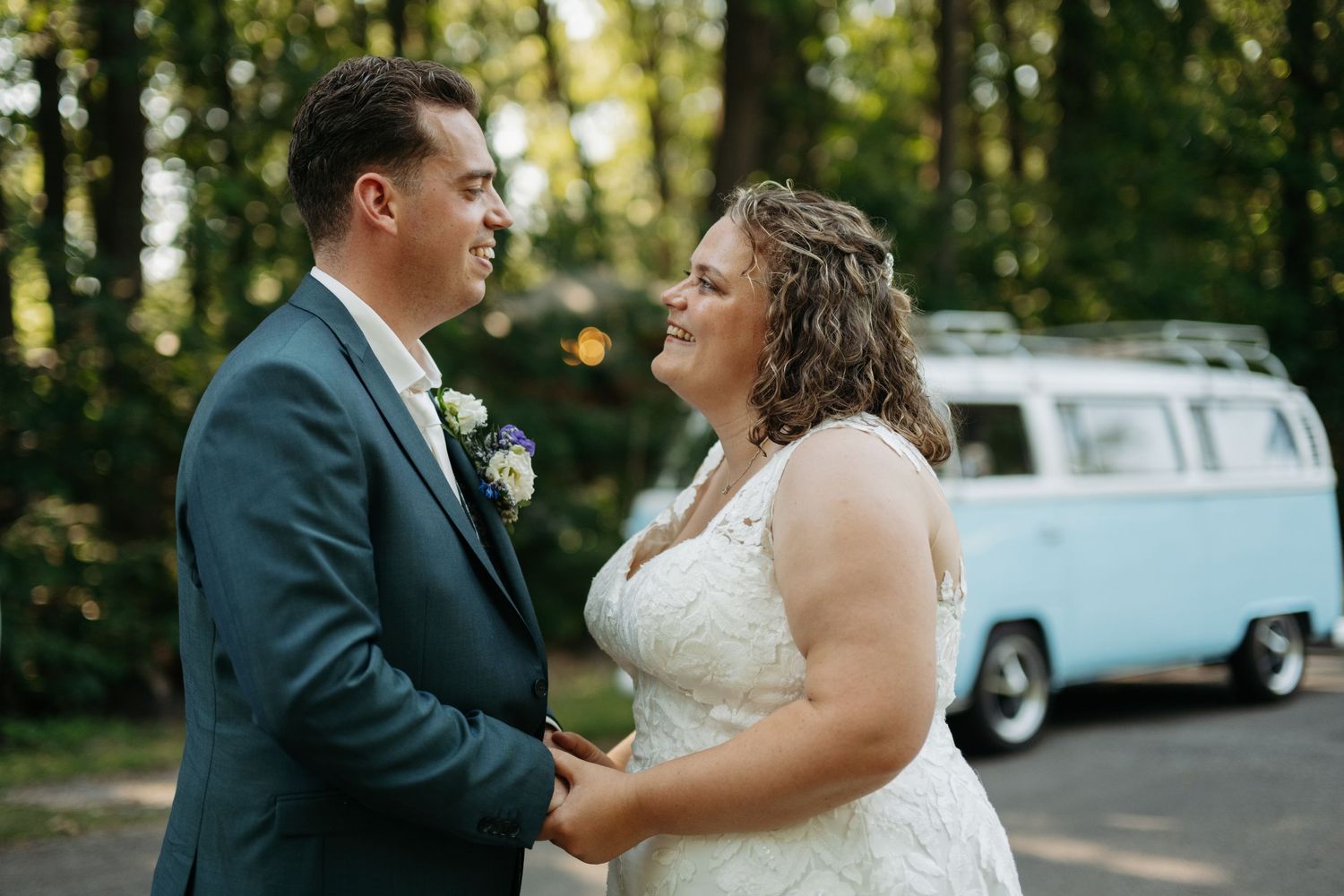 Bride and groom holding hands outdoors with a vintage VW bus in the background.