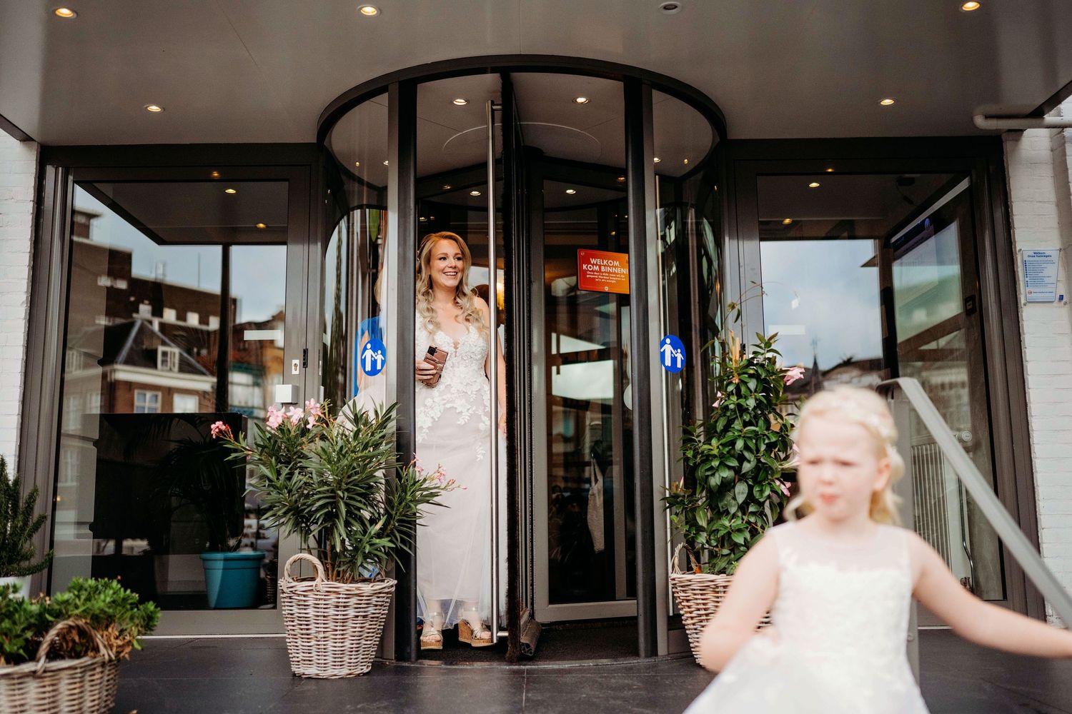 Twee personen in formele kleding bij moderne entree met draaideur, stijlvolle bruidsfotografie in Den Bosch en omgeving Brabant.