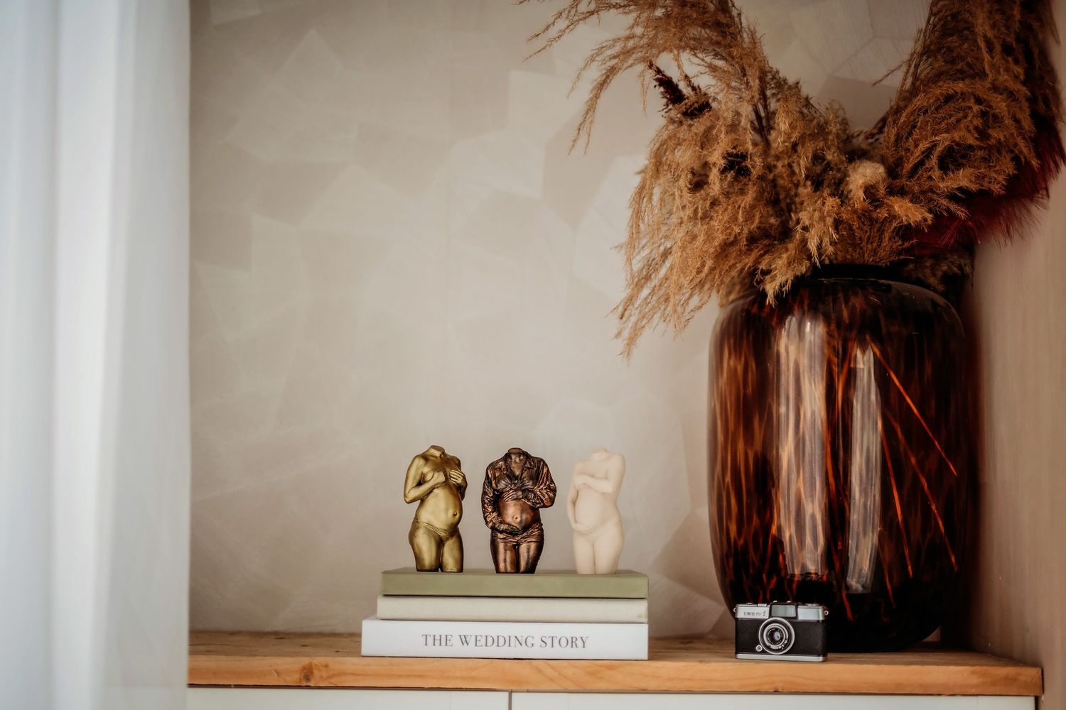 Decorative shelf styling with golden figurines and photography equipment against neutral wall.