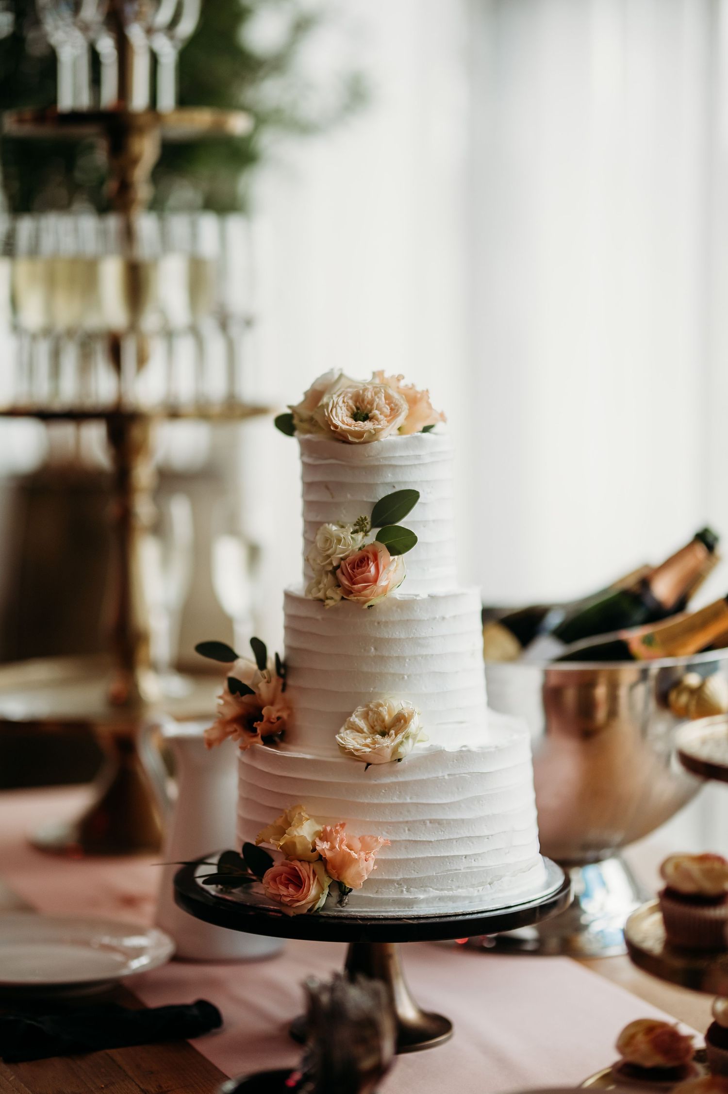 Elegante bruidstaart met textuur en perzikkleurige bloemen op donkere standaard, bruidsfotografie Vught, Brabant.