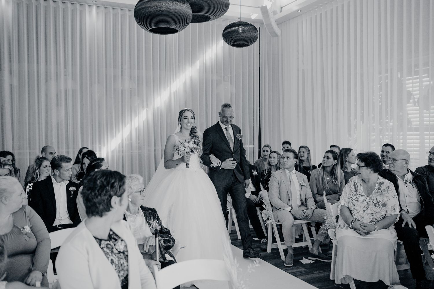 Gasten dansen en socializen in zaal met witte doeken en hanglampen, bruidsfotografie IJM IJzereman Vught, Brabant.