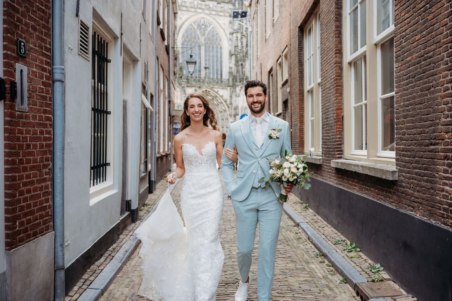 Koppel loopt door een smalle straat met bakstenen tijdens trouwshoot.