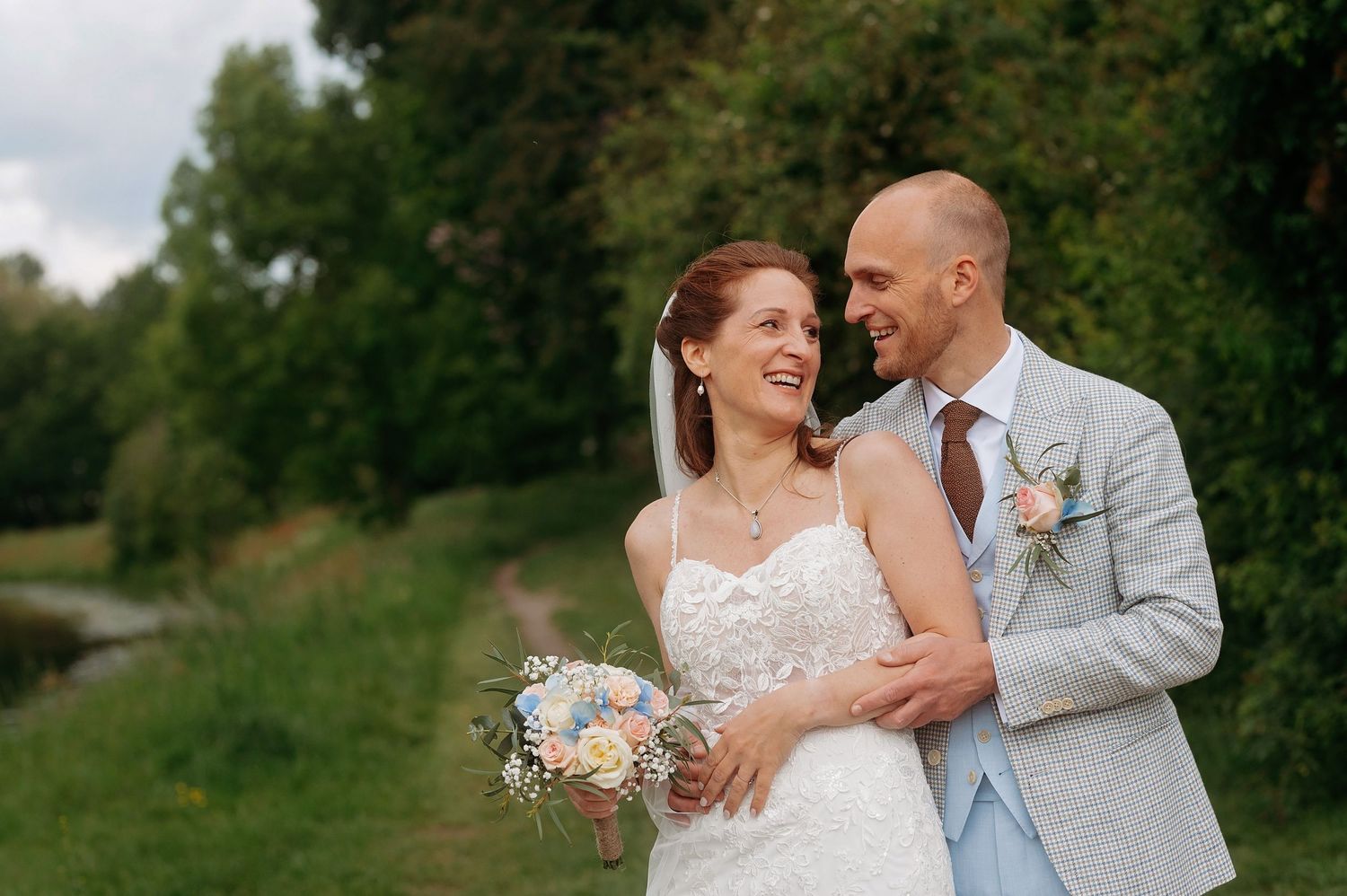 Bride and groom share a romantic moment outdoors, bride holding a pastel bouquet.