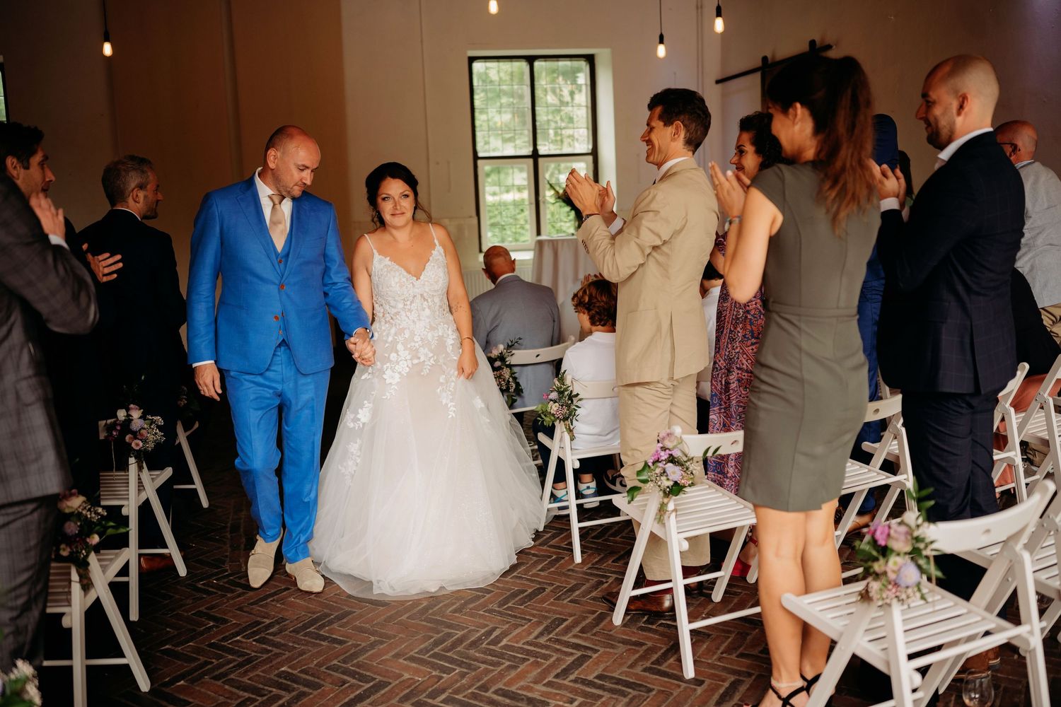 Newlyweds walk down the aisle as guests applaud during their elegant indoor wedding ceremony.