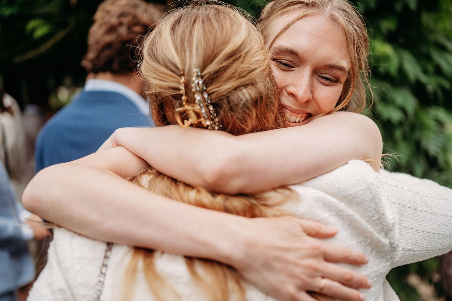 Two blonde women sharing a warm embrace at an outdoor wedding celebration.