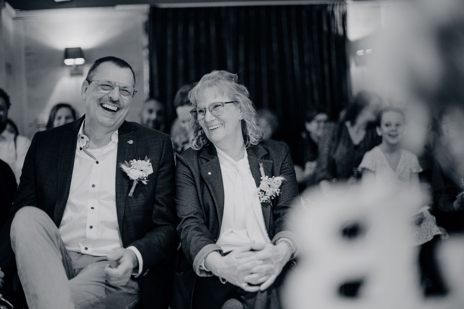 Twee gasten delen spontaan moment binnen, zwart wit bruidsfotografie bij Mr van Eijck Oisterwijk, Brabant.