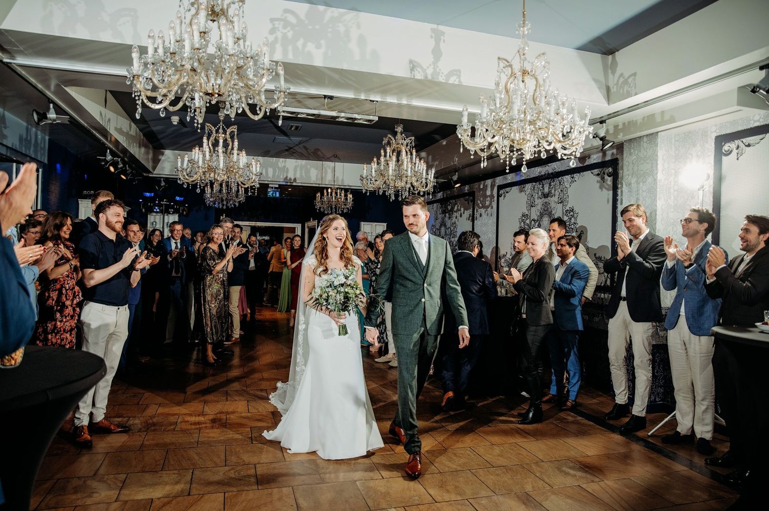 Gasten kijken naar eerste dans van bruidspaar onder kroonluchters, bruidsfotografie Huize Bergen Vught, Brabant.
