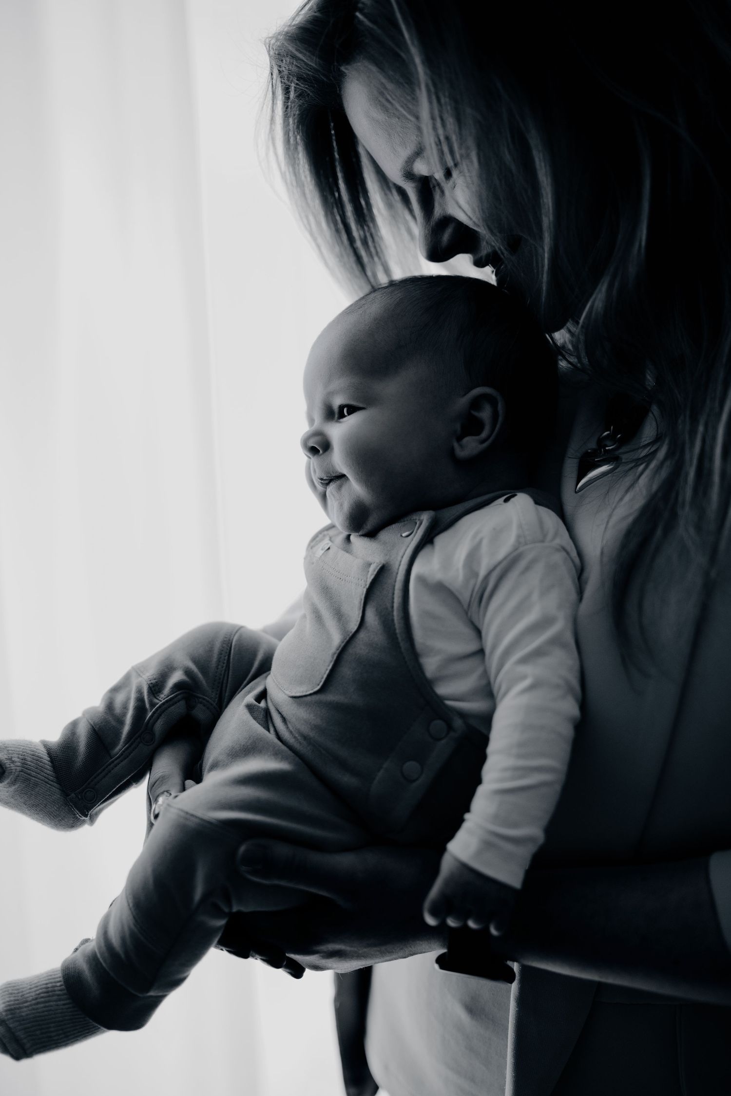 Zwart wit foto van moeder met baby bij raamlicht tijdens newbornshoot in Vught, pure en tijdloze gezinsfotografie