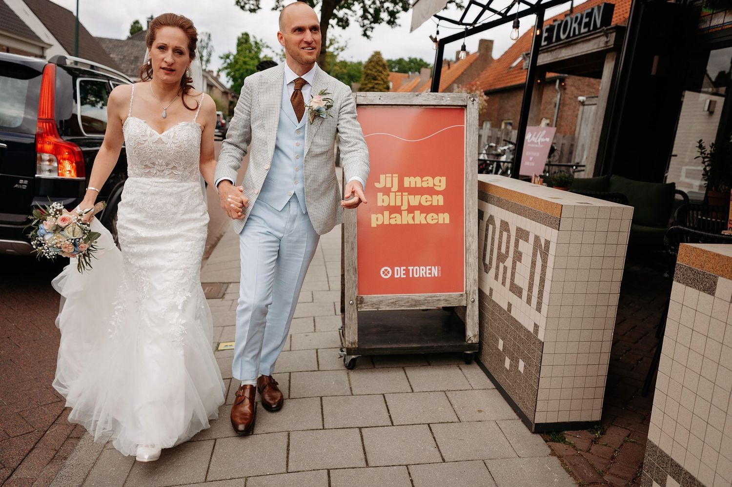 Bride and groom walk together on a sidewalk outside a shop on their wedding day.