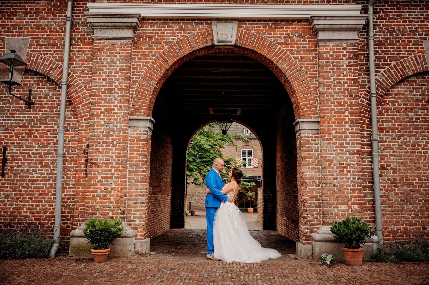 Bride and groom share a romantic moment under a brick archway at an elegant wedding venue.