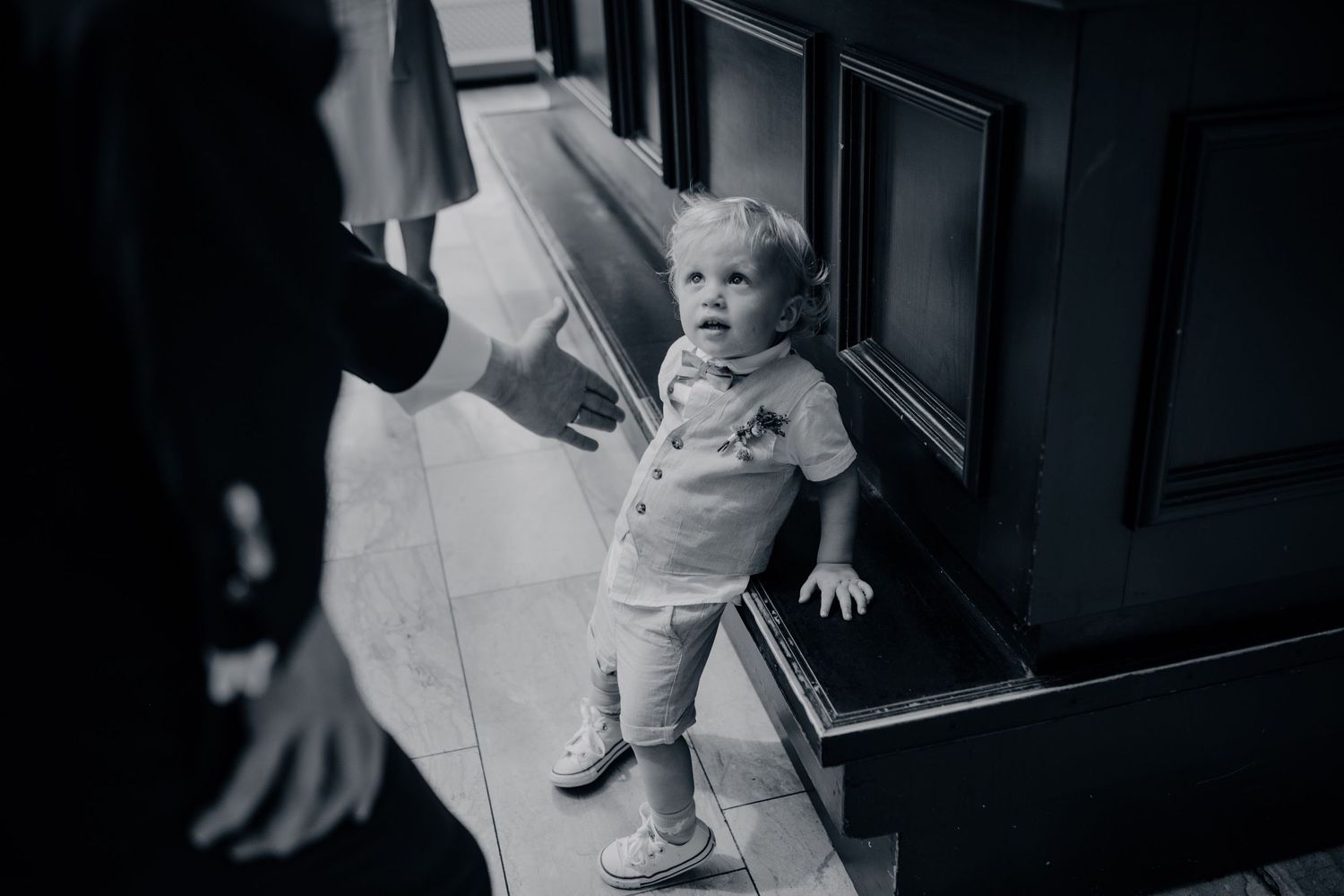 Kind in witte kleding staat bij een deur in zwart-witfoto, artistiek moment voor trouwreportage in Den Bosch.