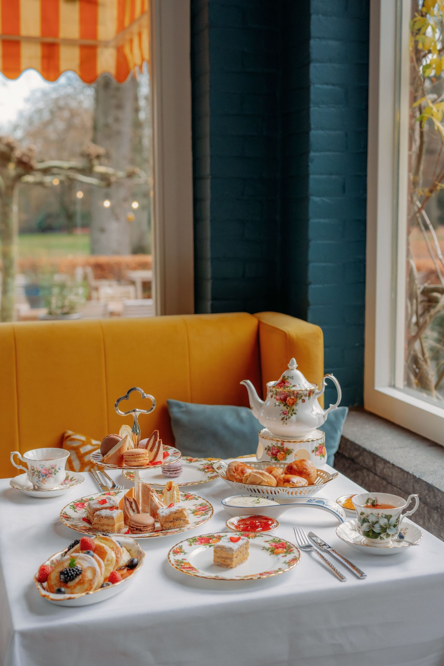High tea met gebak, theepotten en china op wit tafellaken bij raam, foodfotografie Brabant