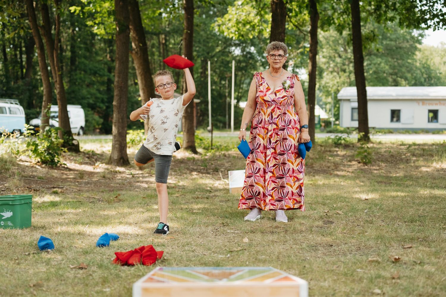 Child and woman playing bean bag toss game outdoors in a sunny park setting during a summer day.