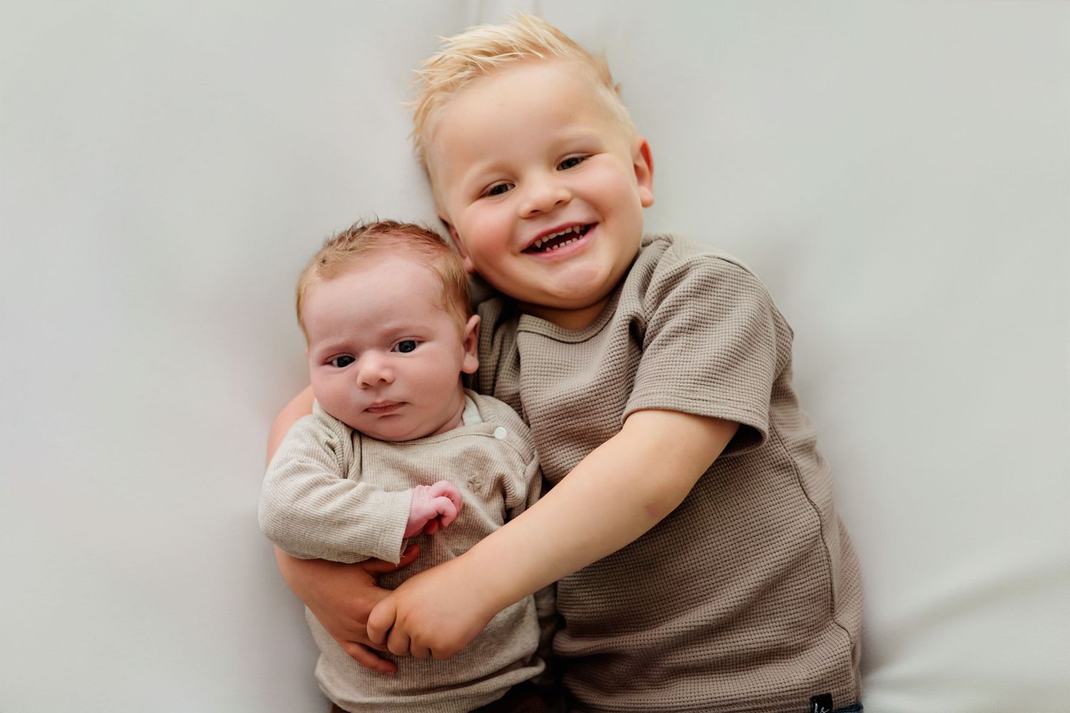 Two siblings sharing sweet embrace on light gray background.